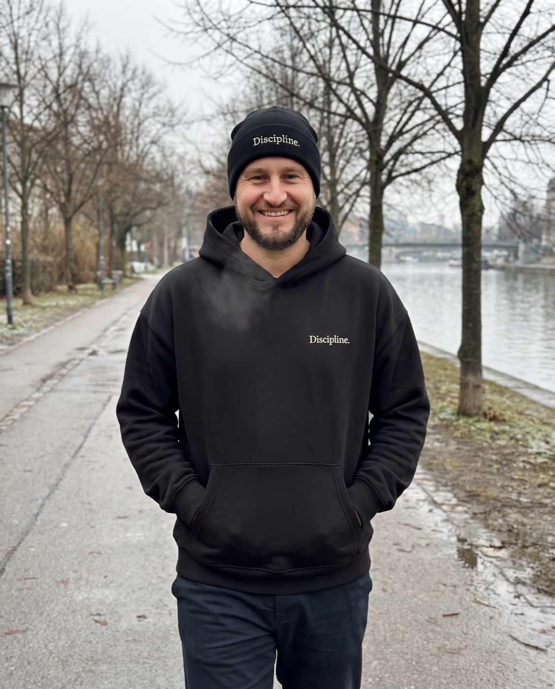 Yves Benini walking along a river path on a cold morning in the black Oversized Hoodie and black Rib Beanie
